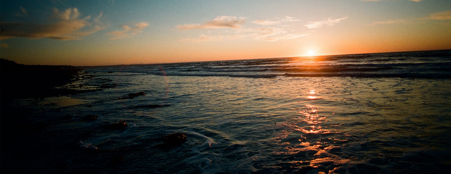 The sun setting into the Pacific over the surf of North Beach, the wet sand glowing orange